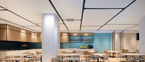 A modern dining area with multiple tables and chairs, a kitchen in the background, and a blue-tiled wall.