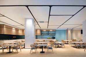 A modern dining area with multiple tables and chairs, a kitchen in the background, and a blue-tiled wall.