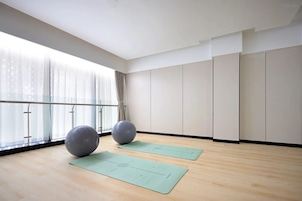 Una habitación amplia con ventanas grandes, suelo de madera, dos balones de ejercicios y dos colchonetas de yoga.