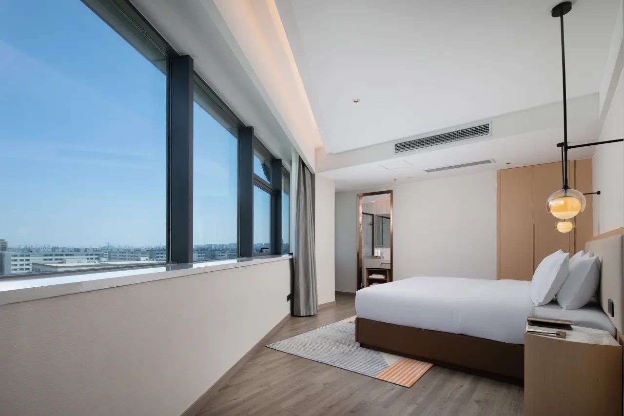 Een moderne hotelkamer met een groot raam, een bed, een nachtkastje en een hanglamp.