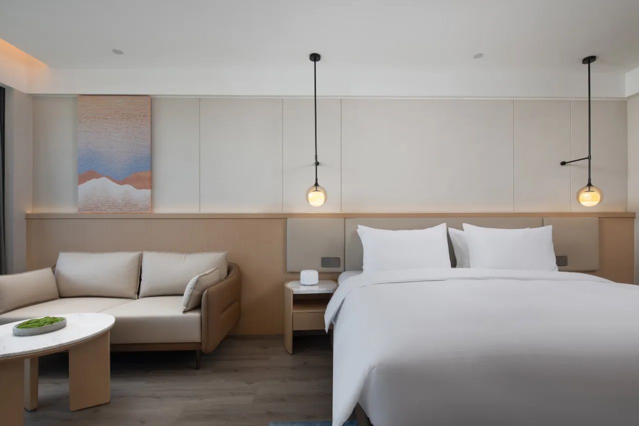 Una habitación de hotel con una cama, un sofá, una mesita y dos lámparas colgantes.