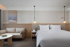 A hotel room with a bed, a sofa, a small table, and two pendant lights. - Novotel Jiaxing Port Area (Jiaxing)