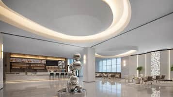 Un vestíbulo moderno con una escultura central, un bar gourmet y zonas de estar.