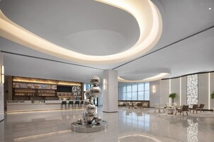 A modern lobby with a central sculpture, a gourmet bar, and seating areas.