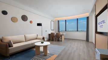 A modern hotel room with a sofa, a small round table, and a view of the city through large windows.