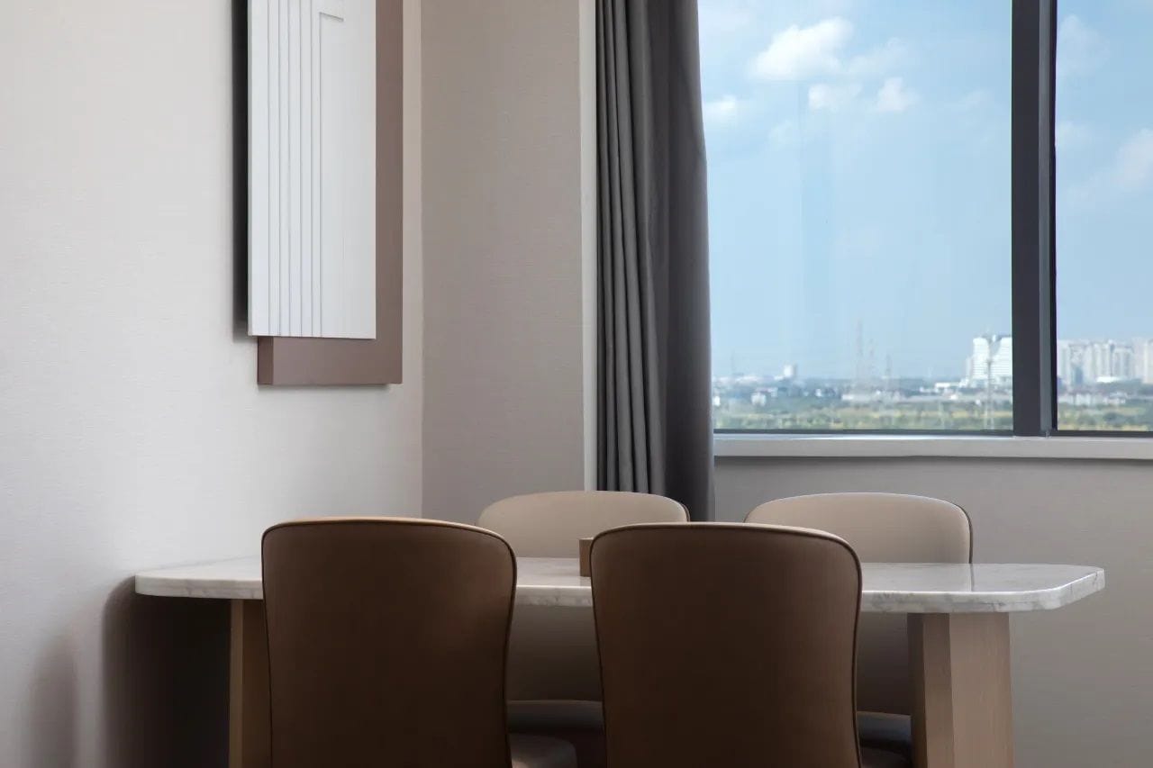 A dining area with a table and chairs, a window with a view of buildings, and a curtain.