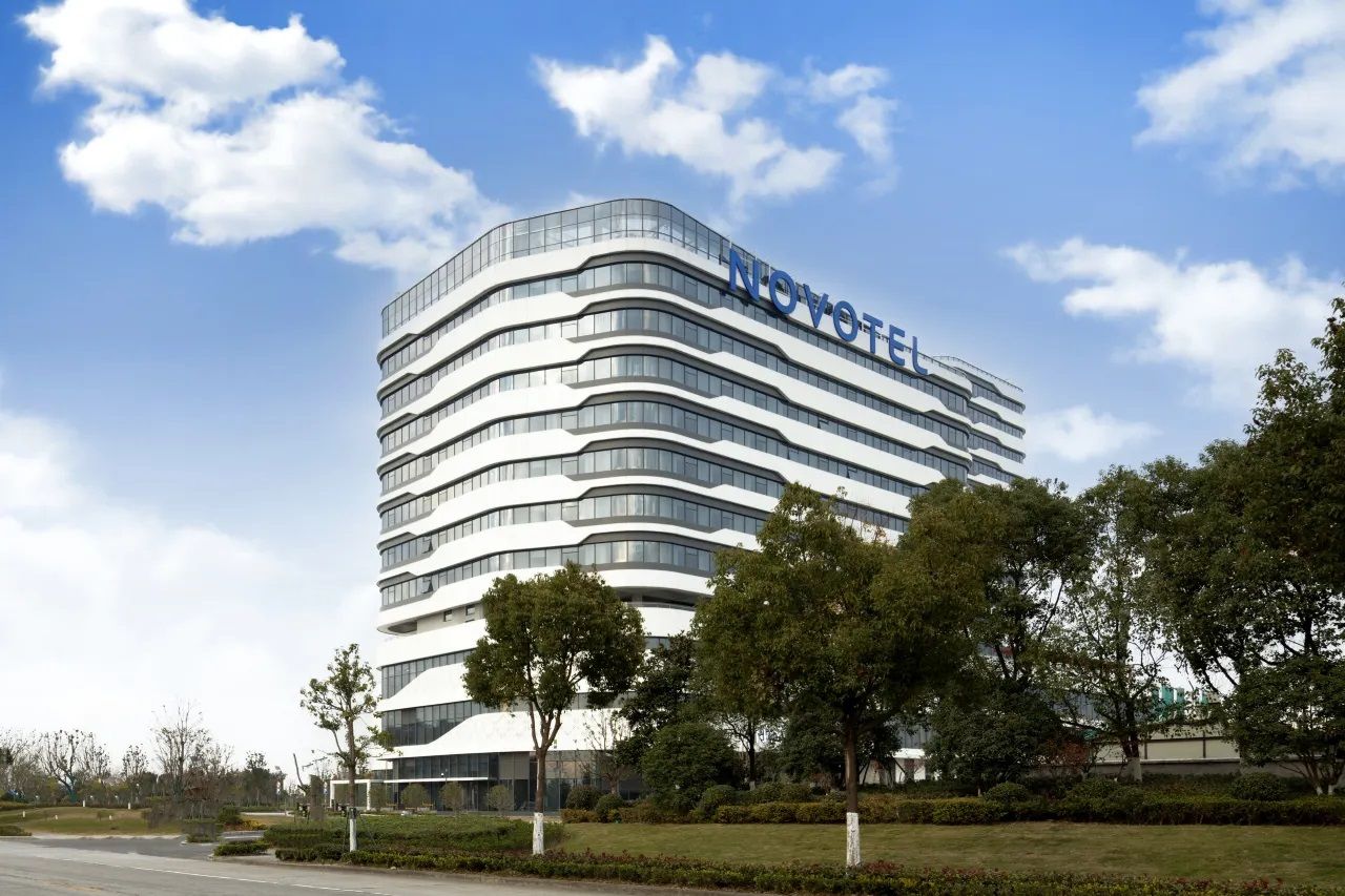 Een modern hotelgebouw met een gebogen gevel en de naam 'NOVOTEL' bovenaan.