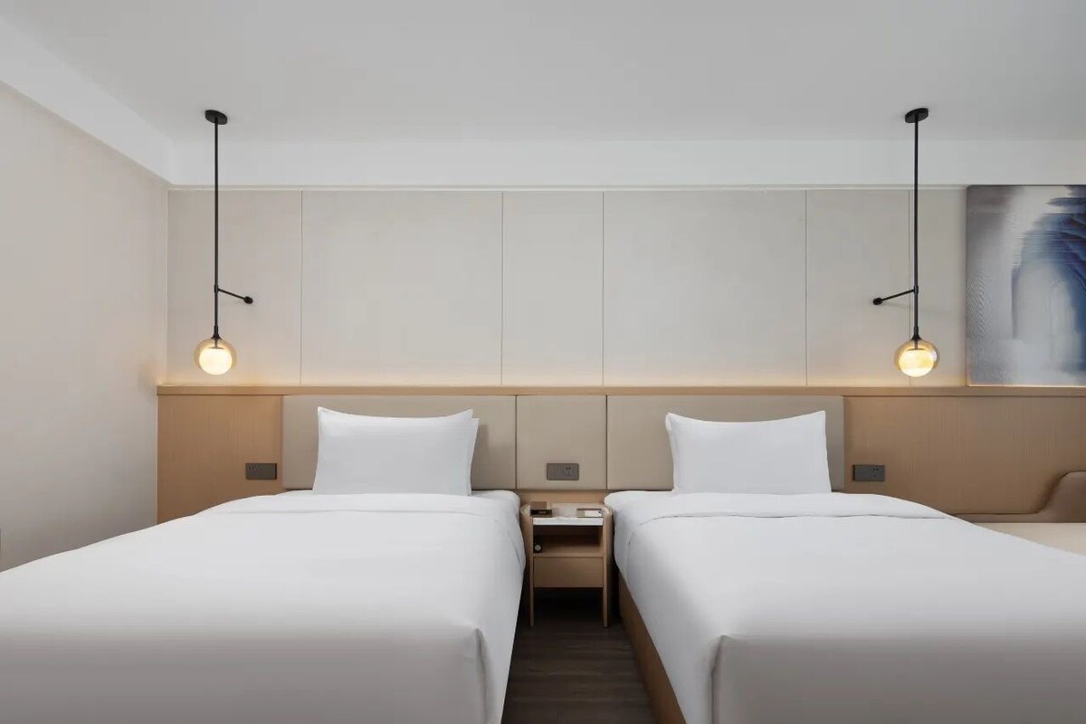 A hotel room with two beds, a nightstand, and a painting on the wall.