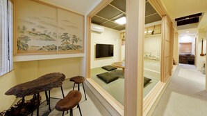 A traditional Japanese room with tatami flooring, a low table with stools, a television, and a sliding door leading to another room. - Residence inn Kamado and Tsuboyu (Osaka)