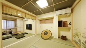 A tatami mat room with a tatami mat table, a tatami mat sofa, a fan, a TV, and a sliding door. - Residence inn Kamado and Tsuboyu (Osaka)