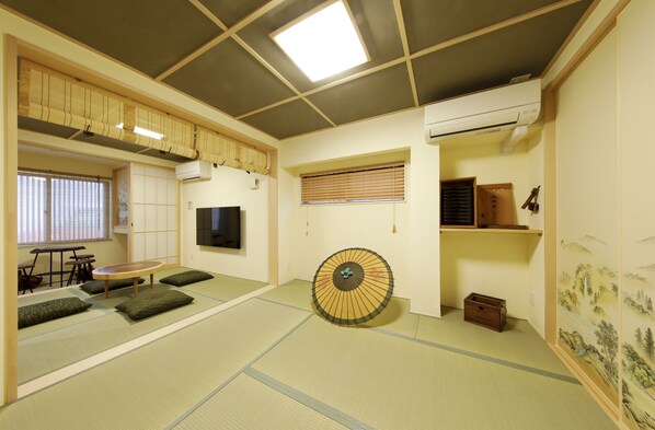 A tatami mat room with a tatami mat table, a tatami mat sofa, a fan, a TV, and a sliding door. - Residence inn Kamado and Tsuboyu (Osaka)