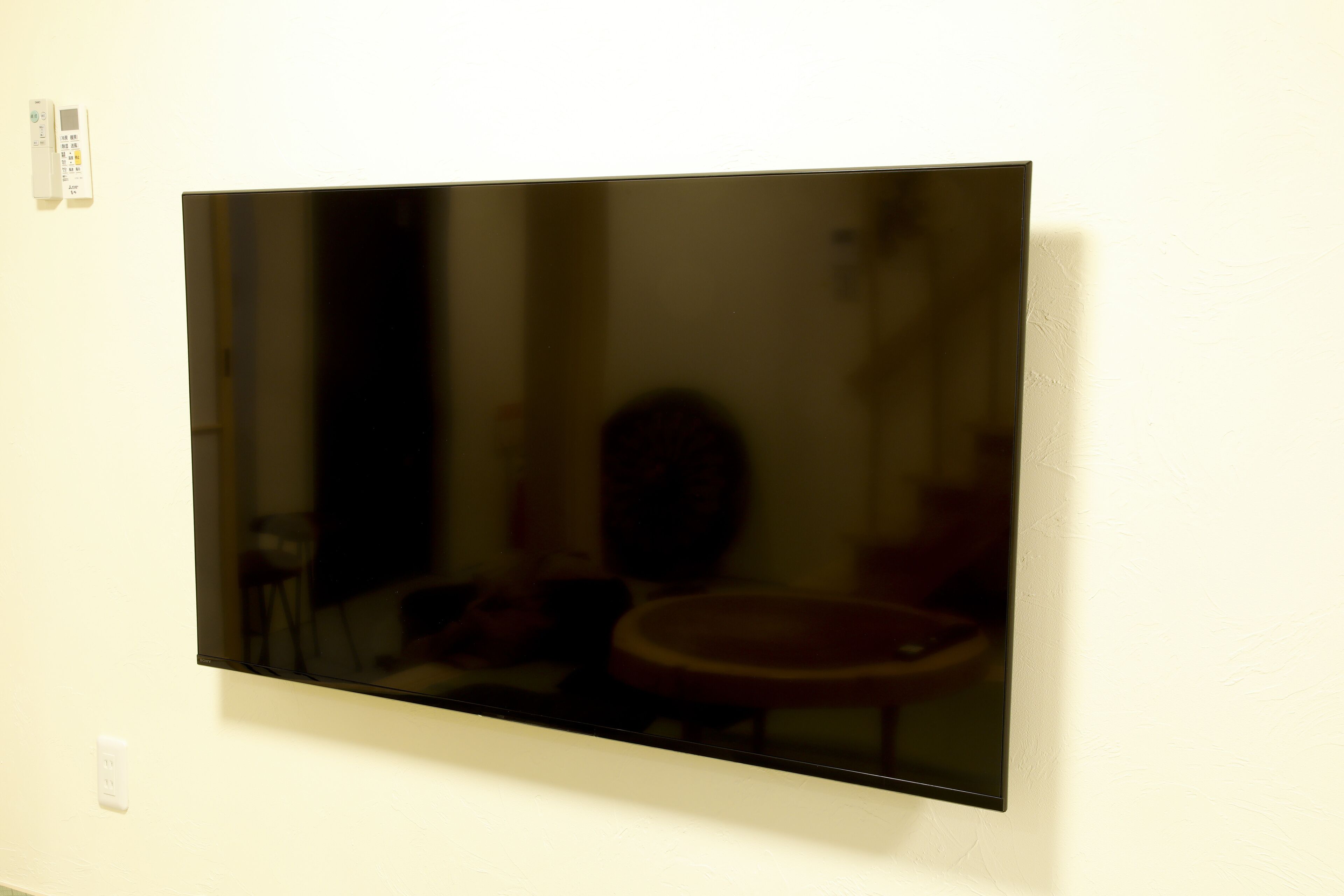 A wall-mounted flat-screen TV in a room with a white wall and a visible electrical outlet.
