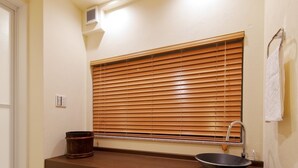 A compact bathroom with a wooden vanity, a sink, and a window with blinds. - Residence inn Kamado and Tsuboyu (Osaka)