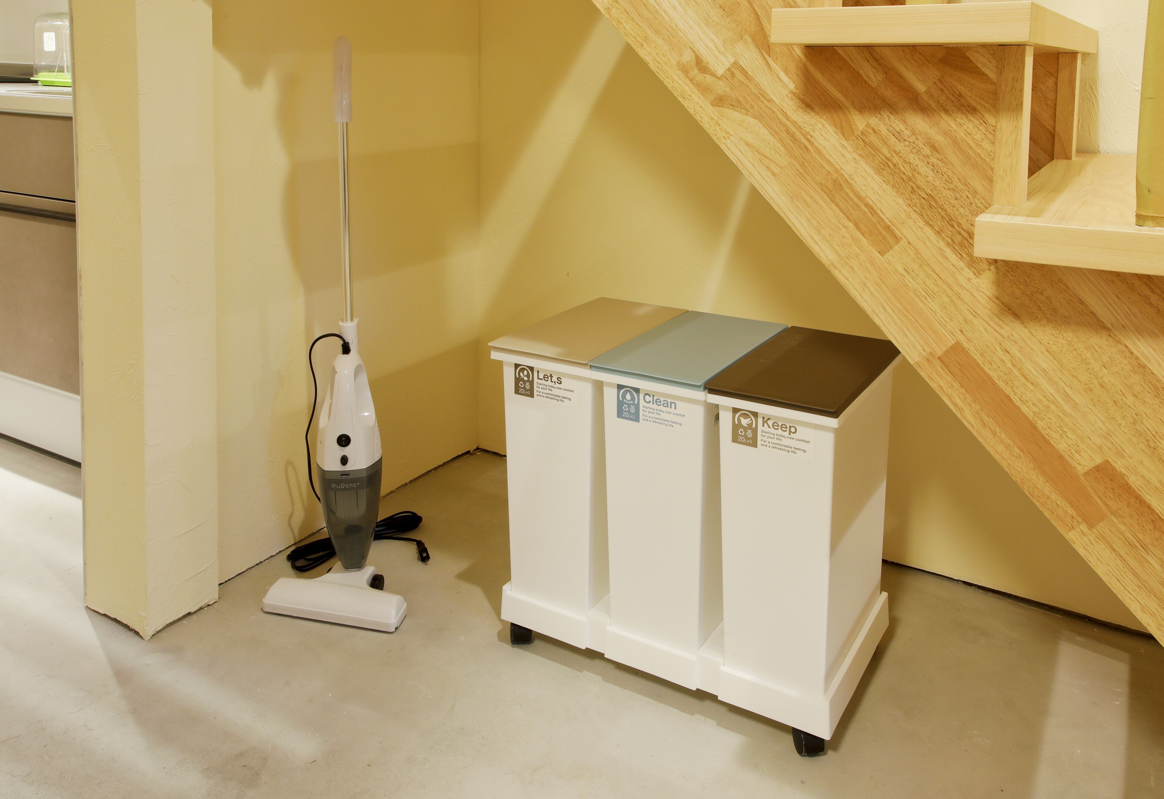 Una habitación con una escalera de madera, un carrito de limpieza blanco y una aspiradora.