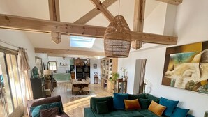 A spacious living area with a large green sofa, a wooden coffee table, and a dining table. There is a large window providing natural light and a view of the kitchen in the background. - Arcachon, La Hume and Dune du Pyla while enjoying a magnificent maison❤️ (Gujan-Mestras)