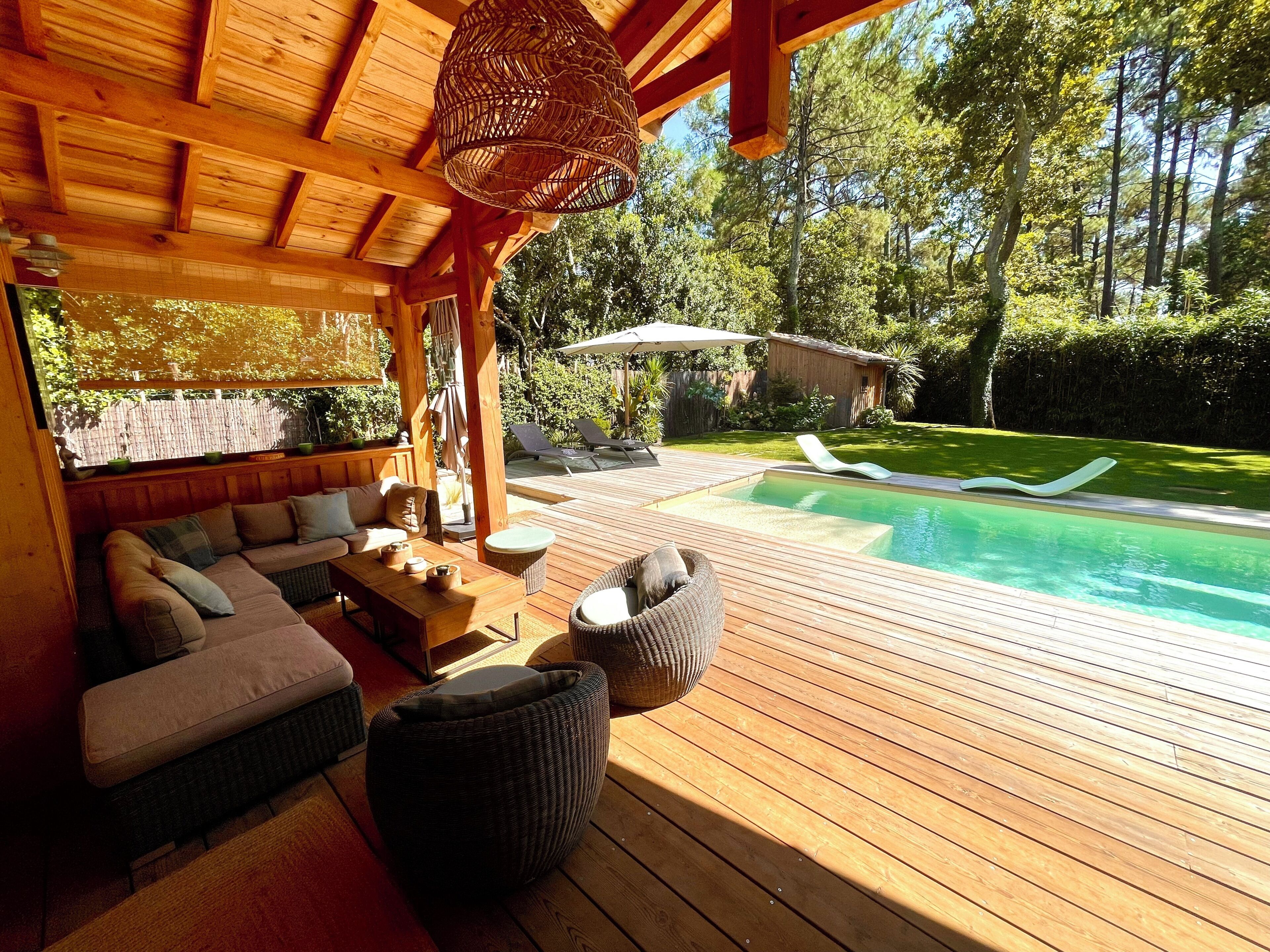 Een houten terras met een zwembad, zitplaatsen buiten en een pergola.