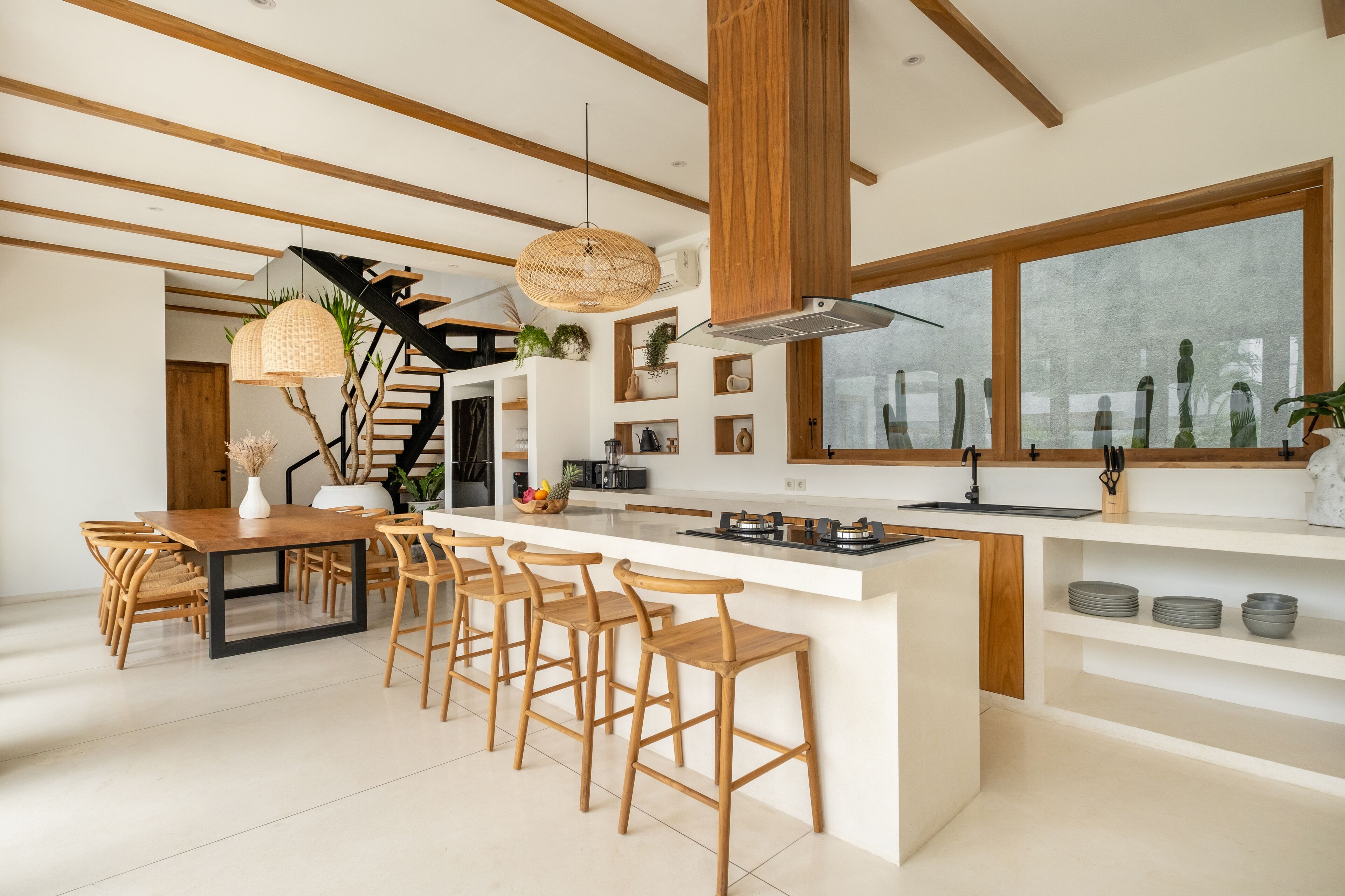 A modern kitchen with a central island, wooden bar stools, and a staircase leading to an upper level.