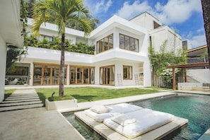 A modern two-story house with a swimming pool, outdoor seating, and a well-maintained lawn.