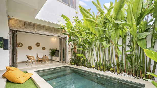 A modern indoor pool area with a clear pool, surrounded by lush greenery and a seating area with a yellow cushion. - Paradise Villa By Hombali (Canggu)