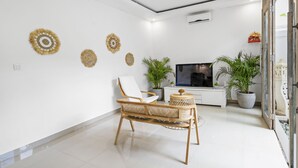 A modern living room with a white sofa, a wicker chair, and a flat-screen TV. There are decorative wall hangings and potted plants. - Paradise Villa By Hombali (Canggu)