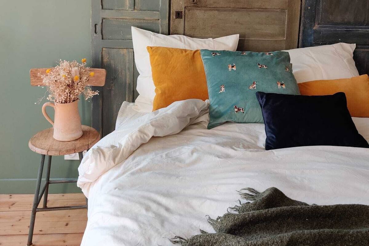 A bed with multiple pillows, a vase with flowers, and a rustic wooden door in the background.