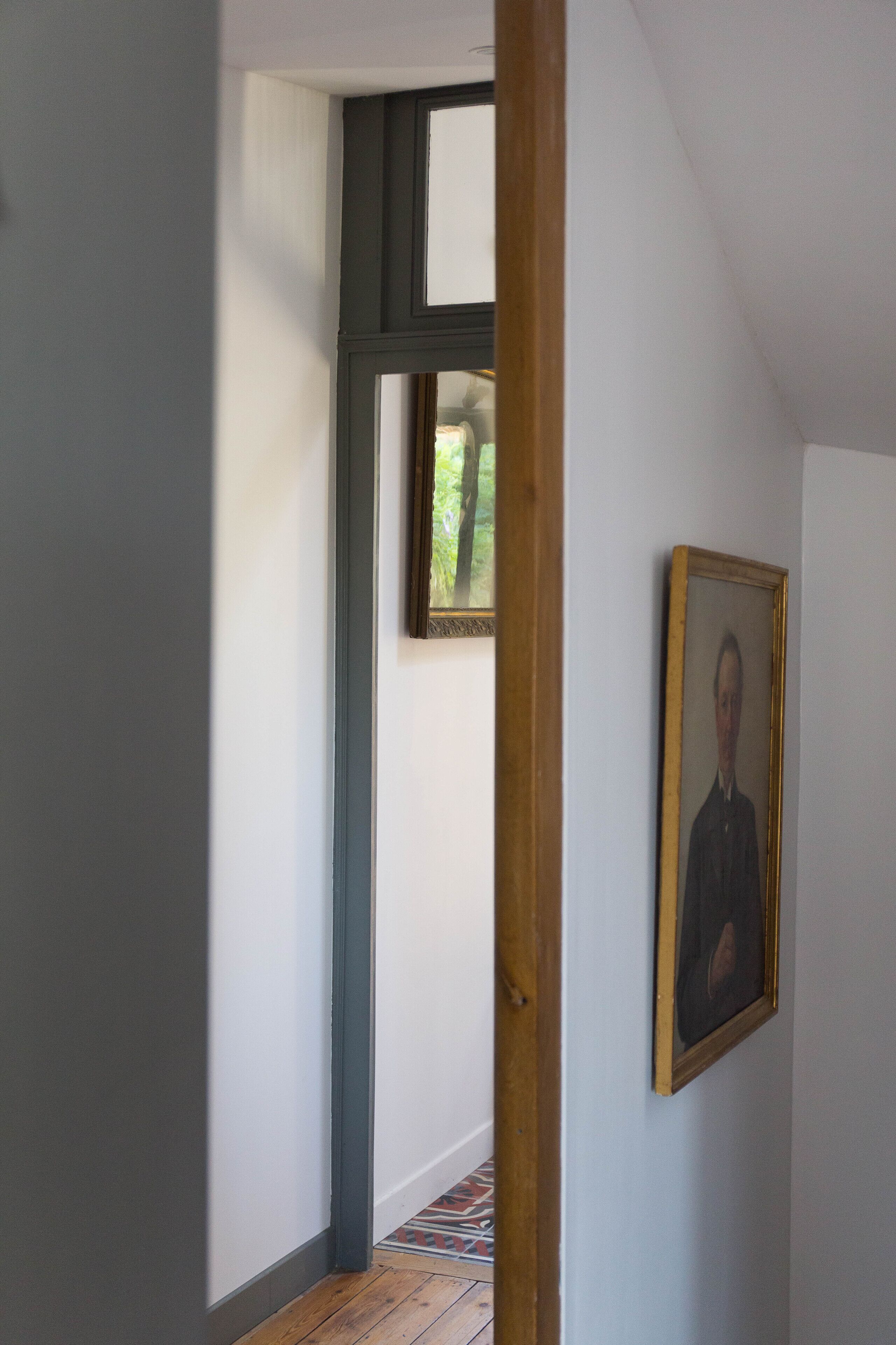A hallway with a wooden door frame, a framed portrait on the wall, and a patterned floor.