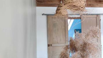 Ein rustikaler Raum mit einer gewebten Pendelleuchte, einer Holztür und einem Bett mit vielen Kissen.