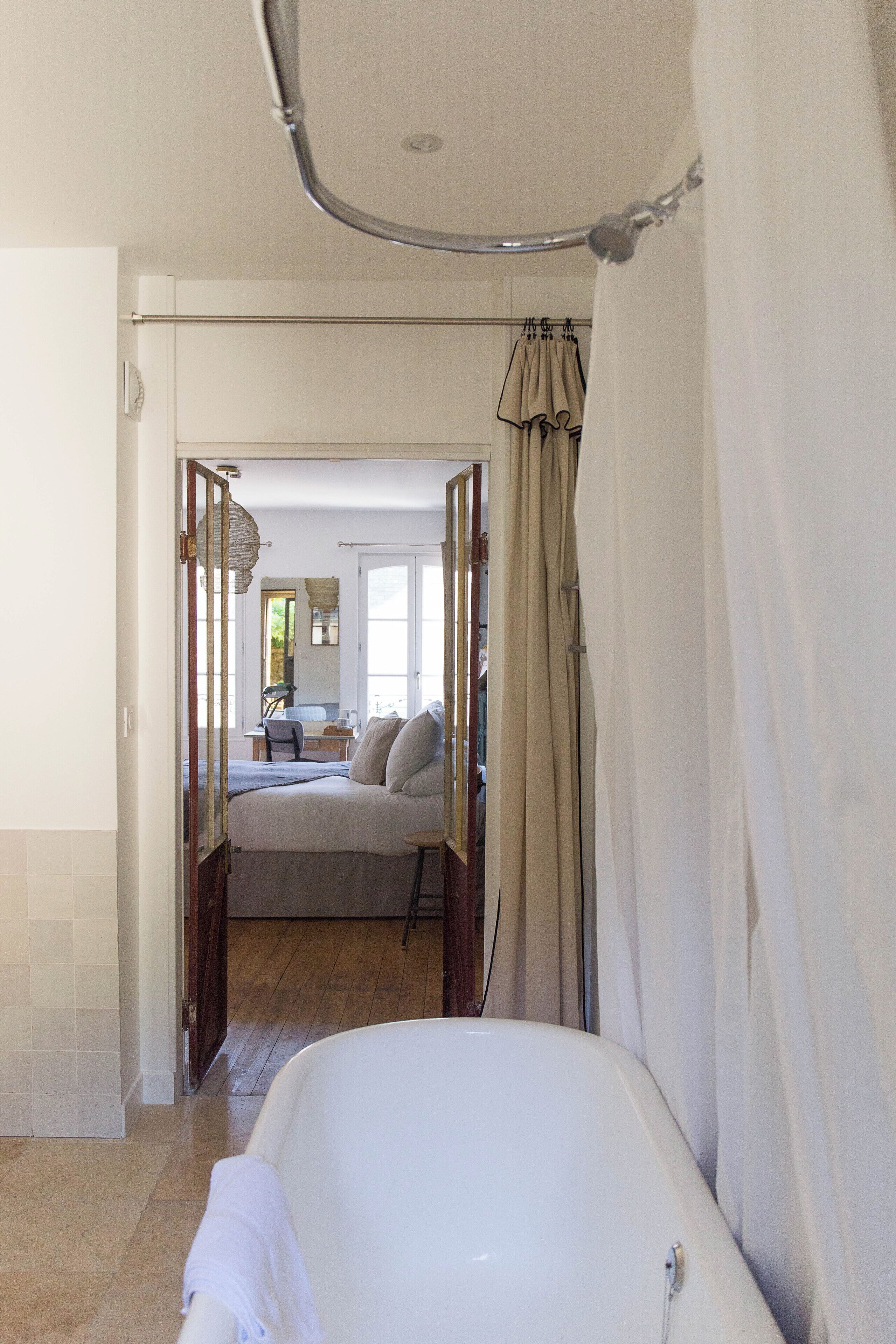 Un baño con bañera, zona de ducha y una puerta que da a un dormitorio con cama y escritorio.