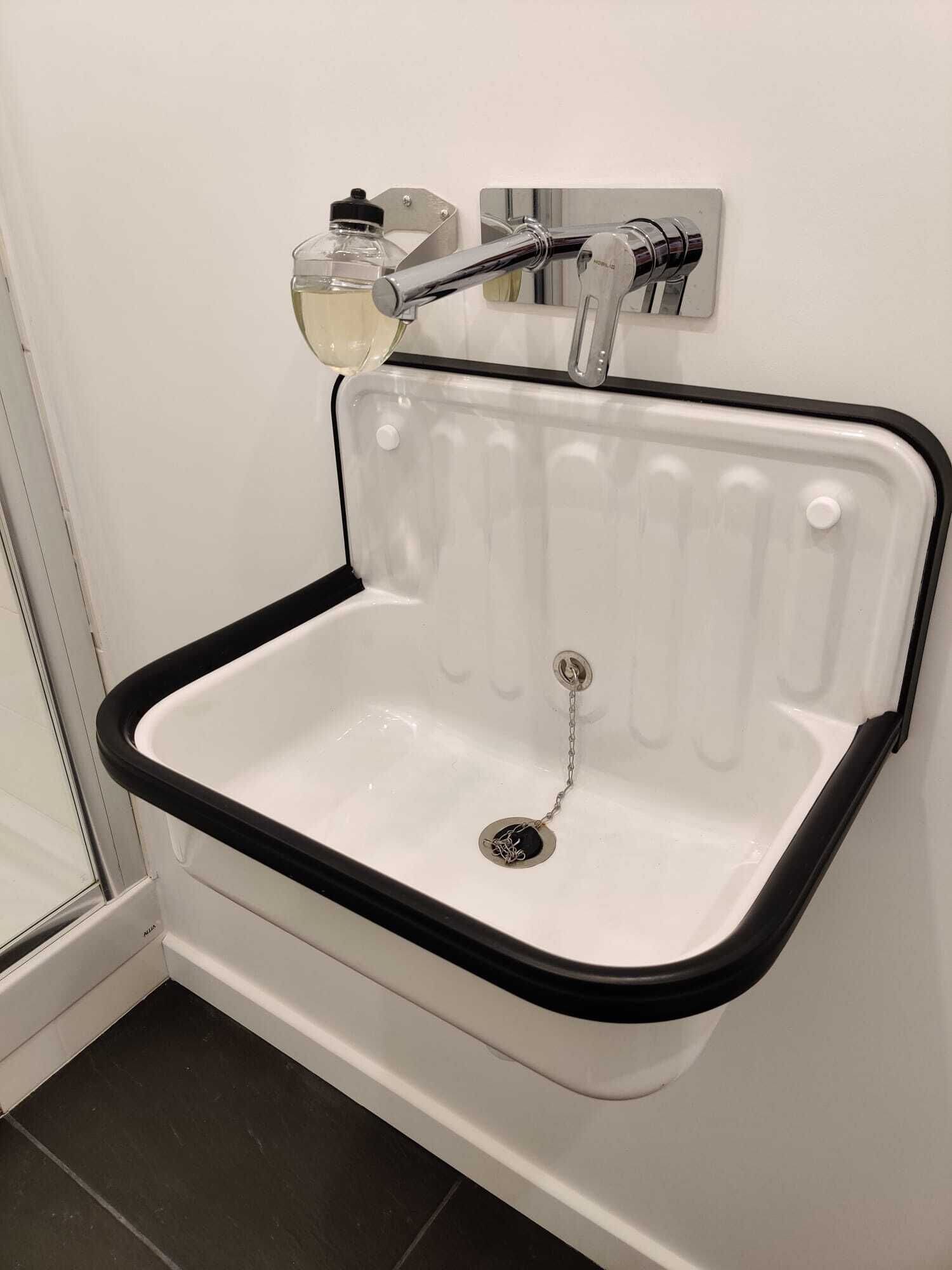 Un lavabo d’angle pour la salle de bain, avec un bord noir et un robinet chromé.
