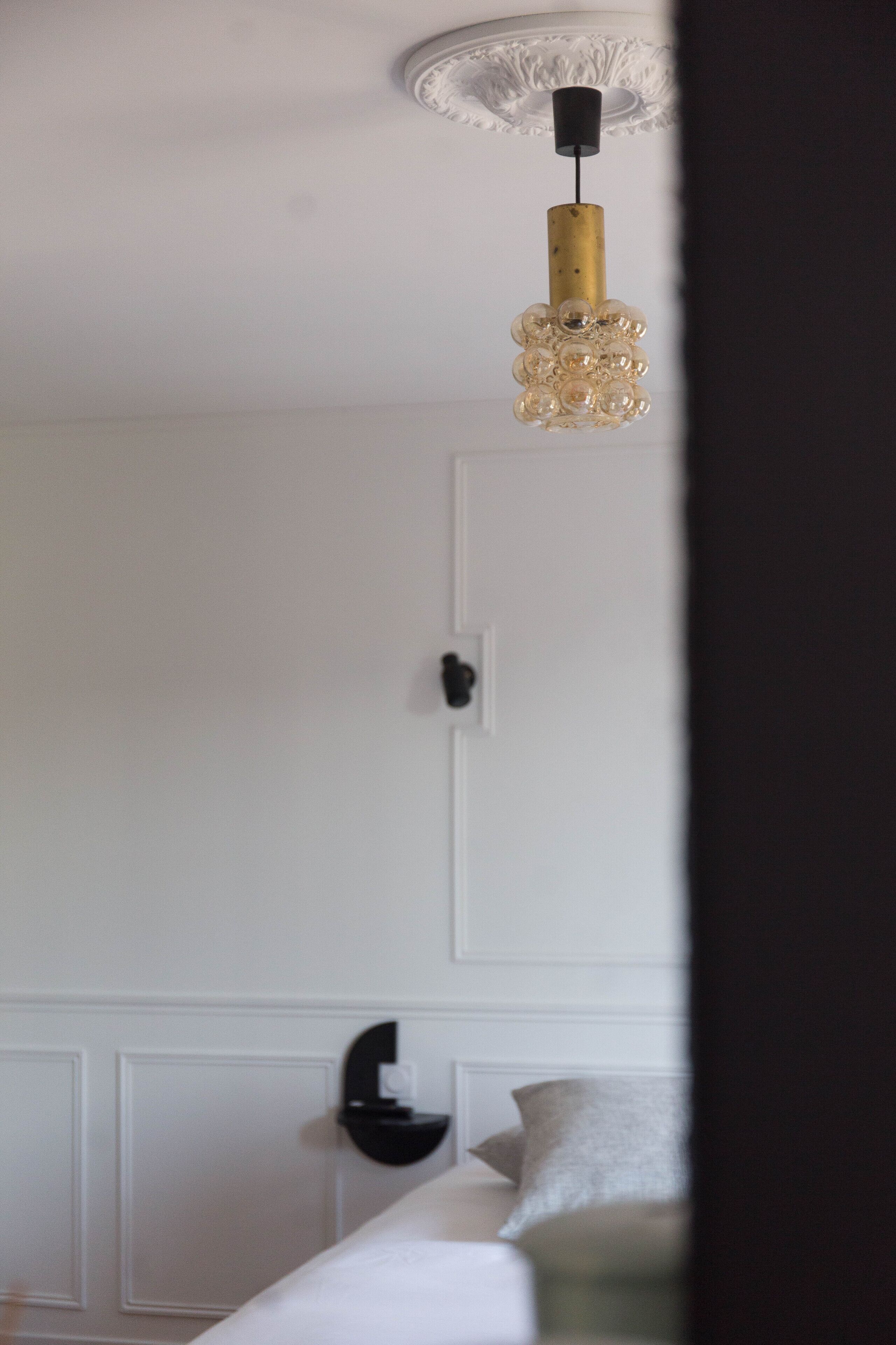Een kamer met een witte muur, een zwart wandlamp en een bed met een wit hoofdeinde en kussens.