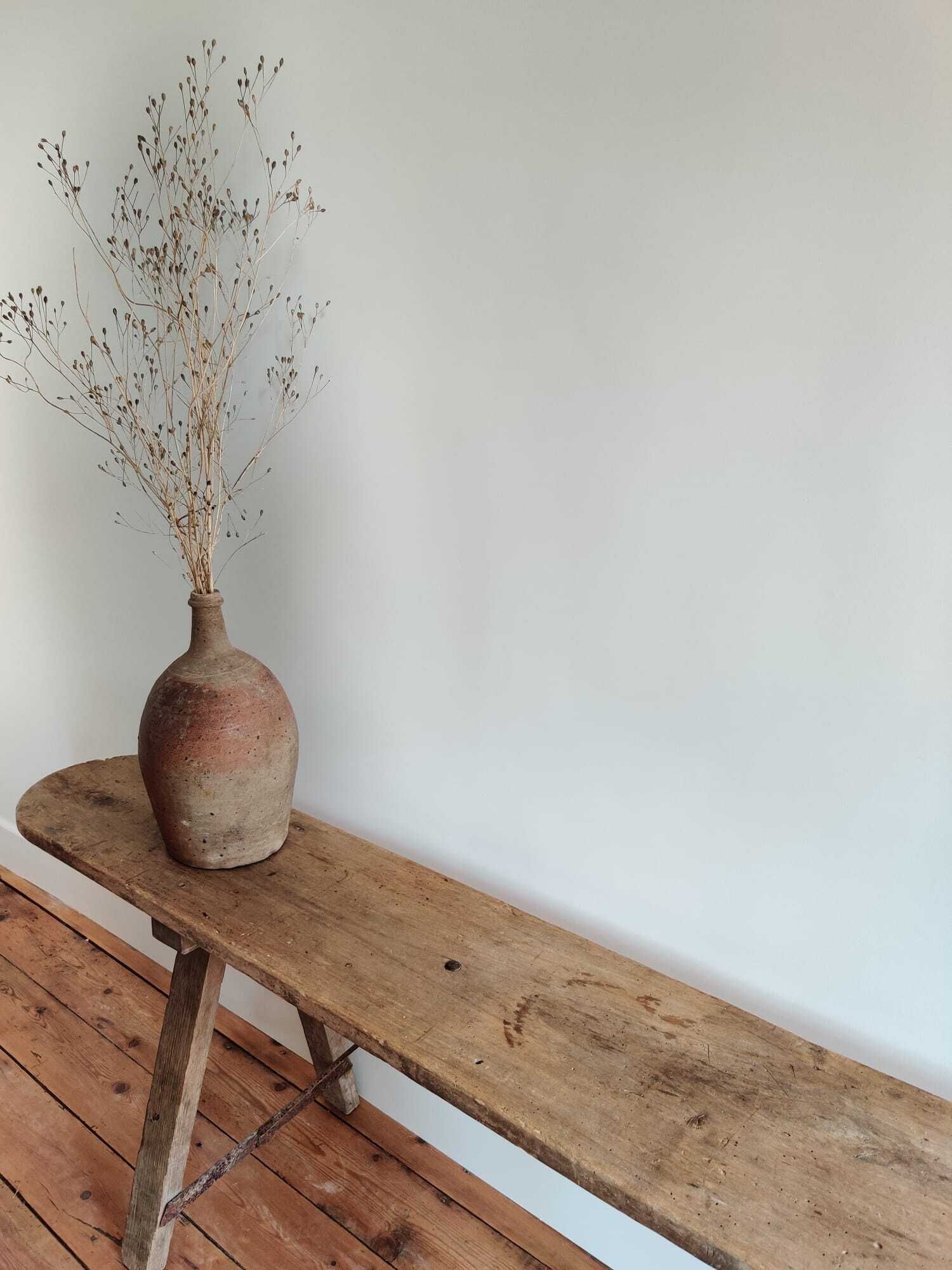 Un banco de madera rústica con un jarrón de plantas secas.