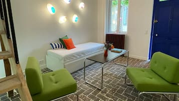 Un salon moderne avec un lit en mezzanine, des fauteuils verts, une table basse en verre et des poutres apparentes.