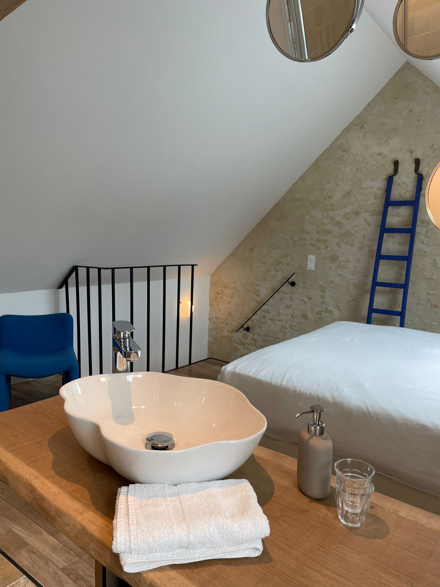 Un baño moderno con un lavamanos tipo pecera, una toalla, un vaso de agua y una escalera apoyada en una pared texturizada.