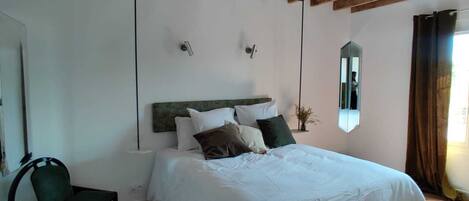 A bedroom with a wooden ceiling, a bed with white bedding, a chair, and a mirror on the wall.