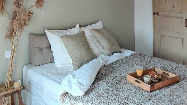 A bedroom with a bed, pillows, a bedside table with a candle, and a tray with breakfast items. - maison seize (Perche-en-Noce)