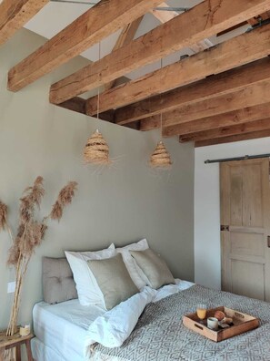 A bedroom with a bed, pillows, a bedside table with a candle, and a tray with breakfast items. - maison seize (Perche-en-Noce)