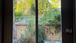 A door with a view of an outdoor patio area with a stone wall, two folding chairs, and a small table. - maison seize (Perche-en-Noce)
