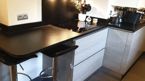 A kitchen with a black countertop, stainless steel appliances, and a coffee machine.