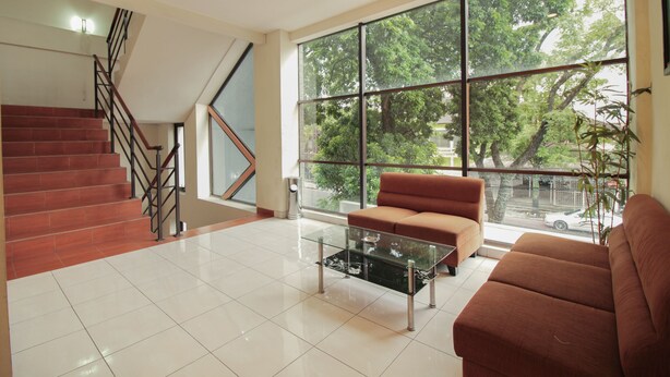 A spacious living area with a staircase, a large window offering a view of trees, and a brown sofa. - Capital O Galaxy Inn (Bandung)