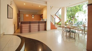 A hotel lobby with a reception desk, a staircase, and a dining area with tables and chairs. - Capital O Galaxy Inn (Bandung)
