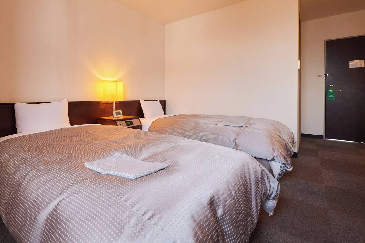 A hotel room with two beds, a nightstand, a lamp, and a door.