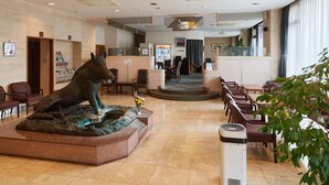 Un vestíbulo de hotel con una escultura central, zonas de estar y una mesa de recepción.