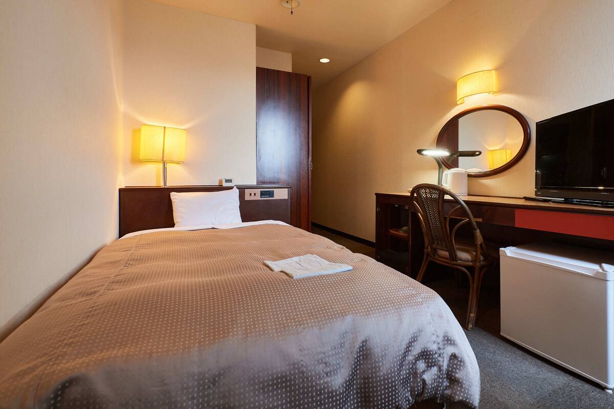 A hotel room with a bed, desk, chair, TV, and a mirror.