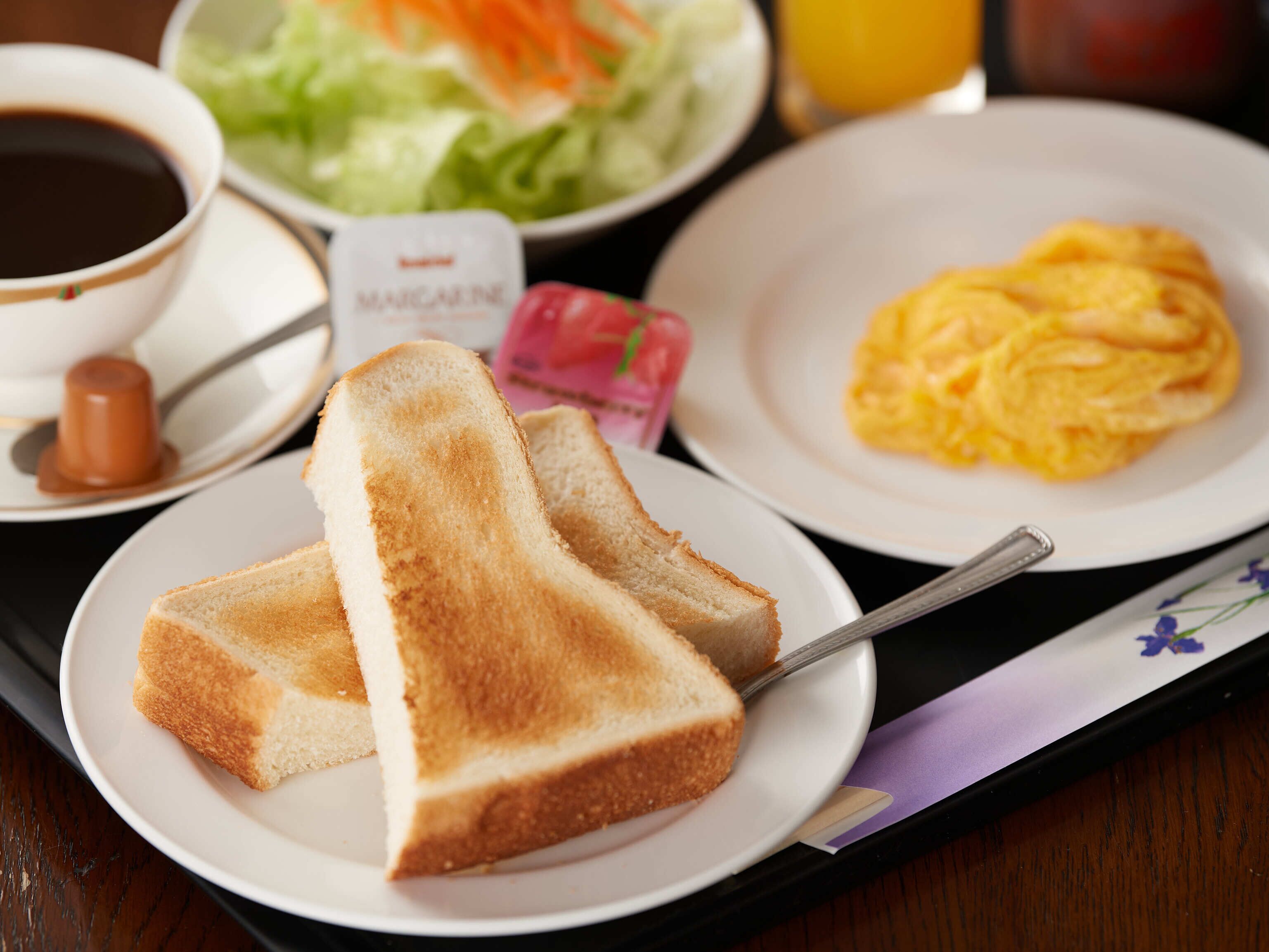 A breakfast tray with toast, scrambled eggs, a cup of coffee, a salad, and a bottle of sauce.