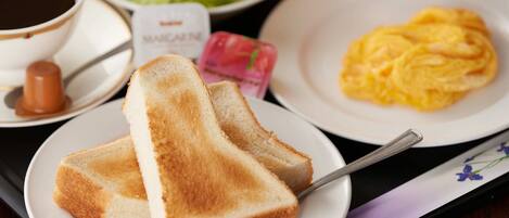 A breakfast tray with toast, scrambled eggs, a cup of coffee, a salad, and a bottle of sauce.