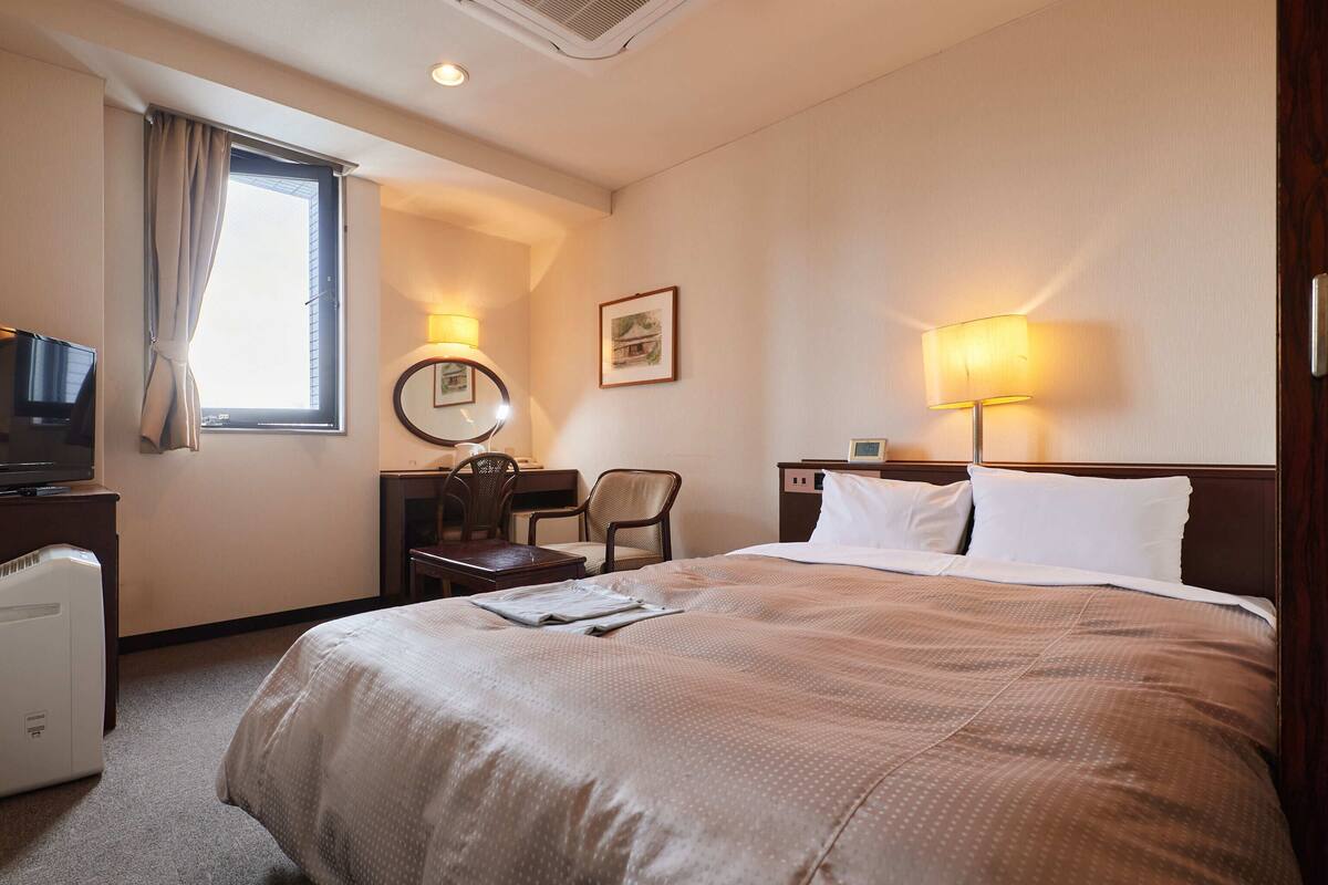 A hotel room with a large bed, a desk with a chair, a television, and a window with curtains.