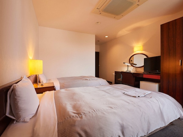 A hotel room with two beds, a desk with a lamp, a mirror, and a television.