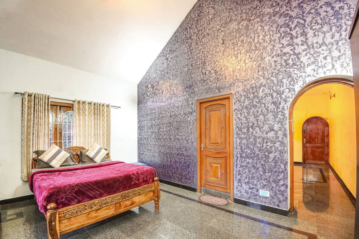 A bedroom with a wooden bed, a window with curtains, a patterned wall, and a wooden door.