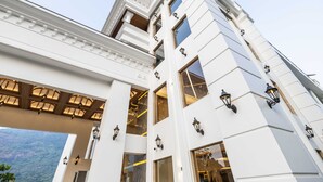 A multi-story building with a classical architectural style, featuring prominent columns, large windows, and decorative lighting fixtures. - The Grand Cliff Resort Munnar  (Devikolam)