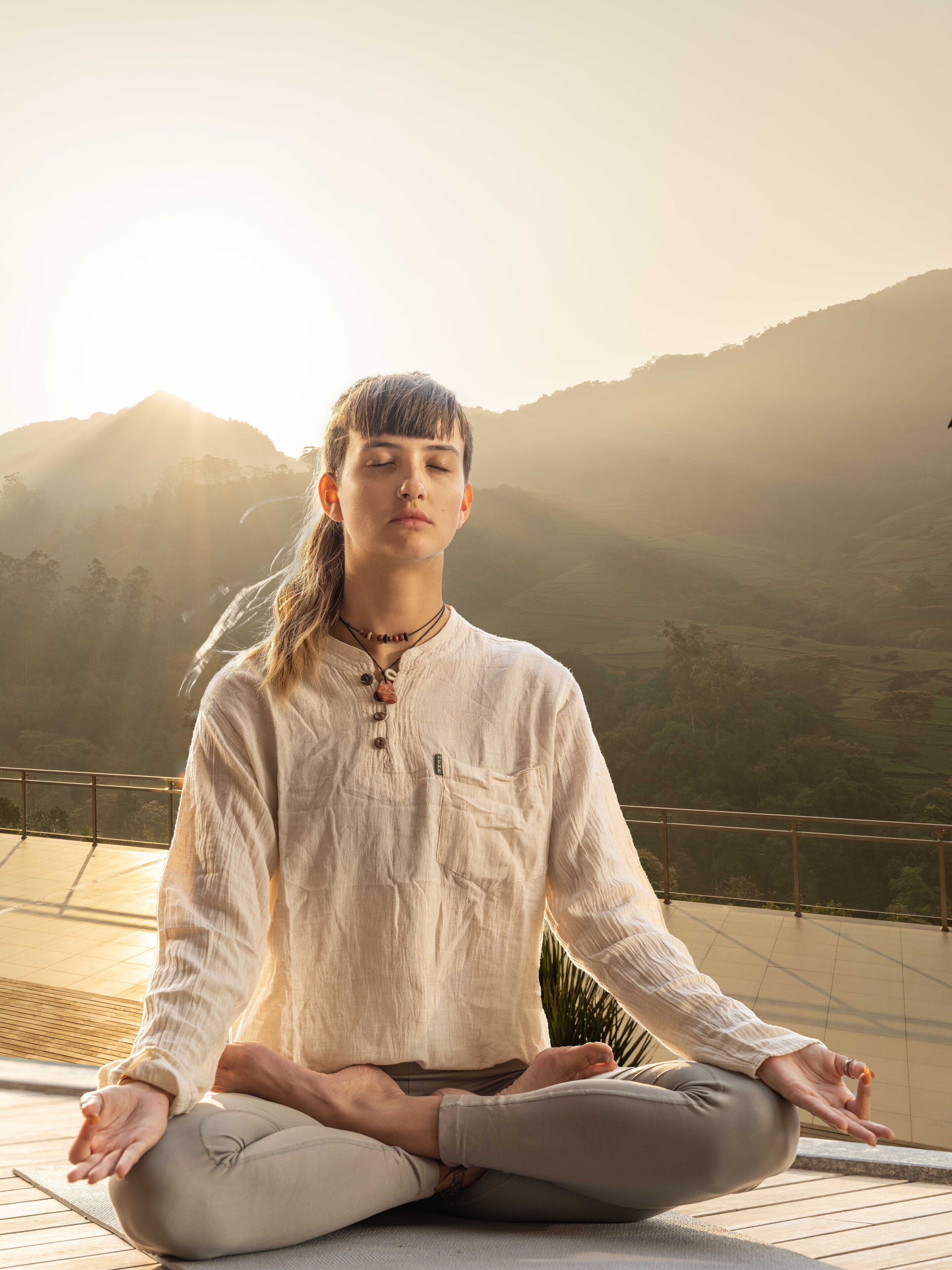 A person meditating on a wooden deck with a mountainous landscape in the background.